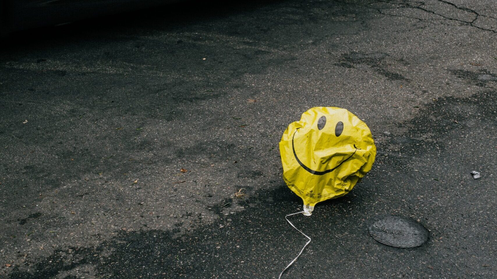 smiling emoji balloon beside black car during daytime
